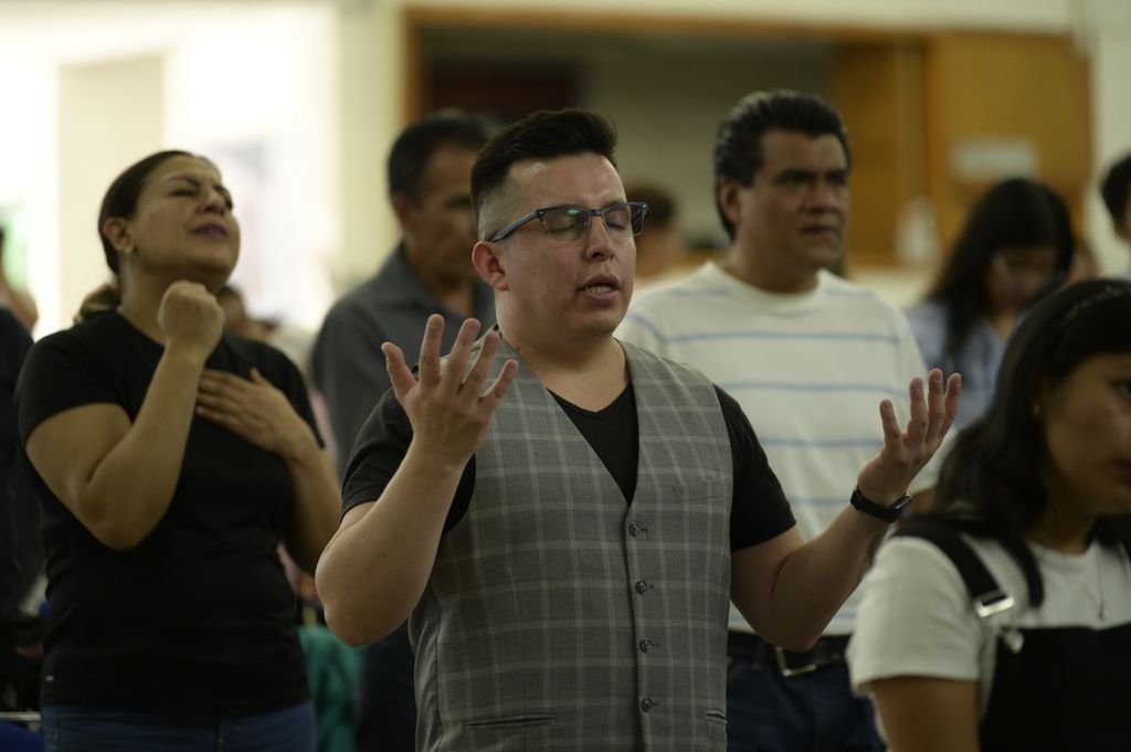 A diverse group of adults praying together indoors in Ciudad de México.